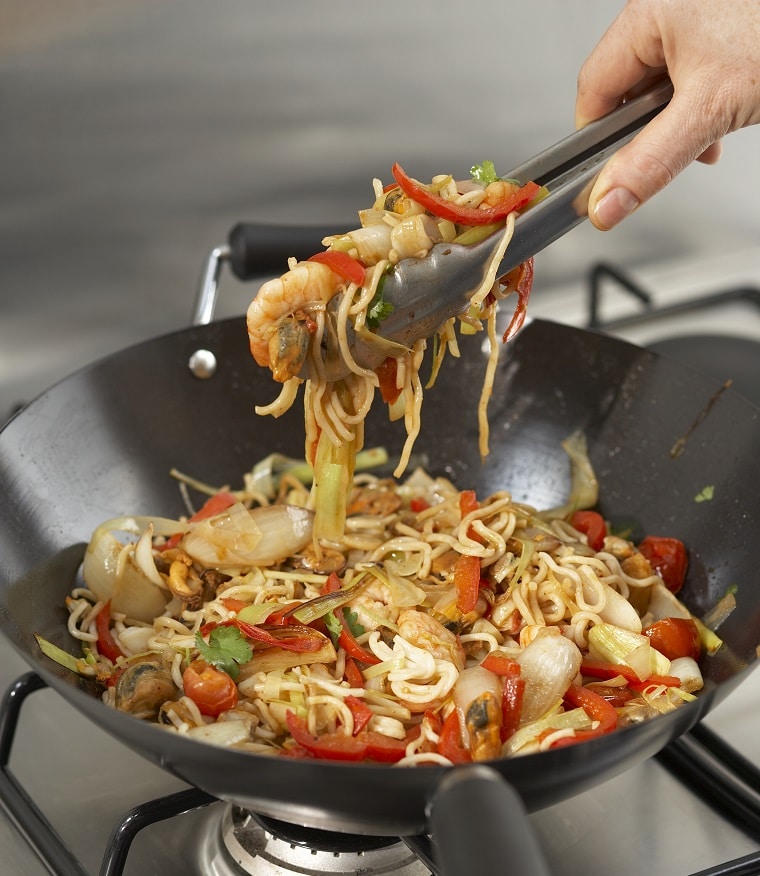 A person taking out fried stir fry seafood with noodles of a pan