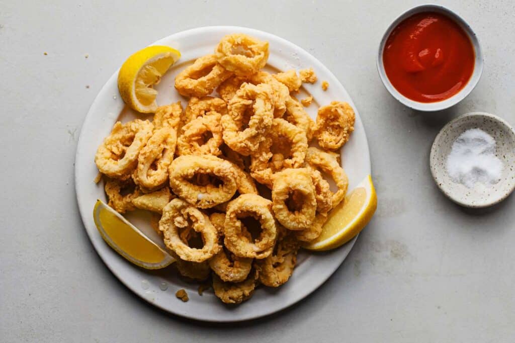 A top view of calamari plated out with lemons and ketchup and salt