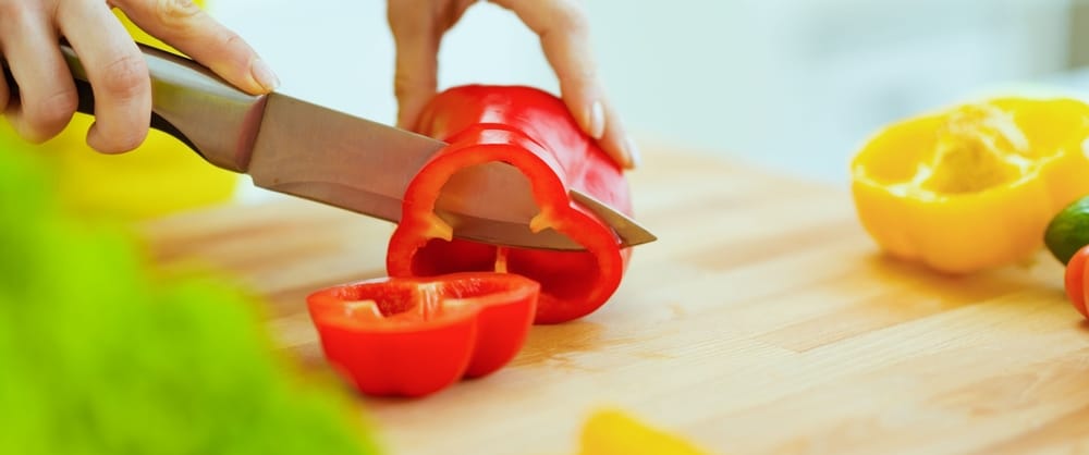 A view of a hand cutting red bell peppers