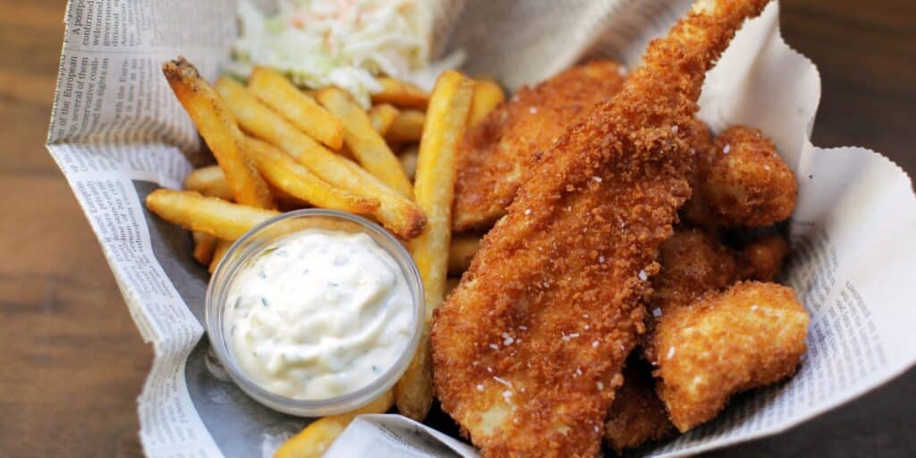 A view of fried fish and chips in a newspaper served with white dip sauce