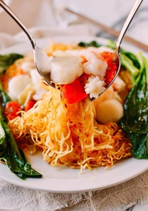 A view of two spoons holding out the seafood pan fried noodles out of a plate