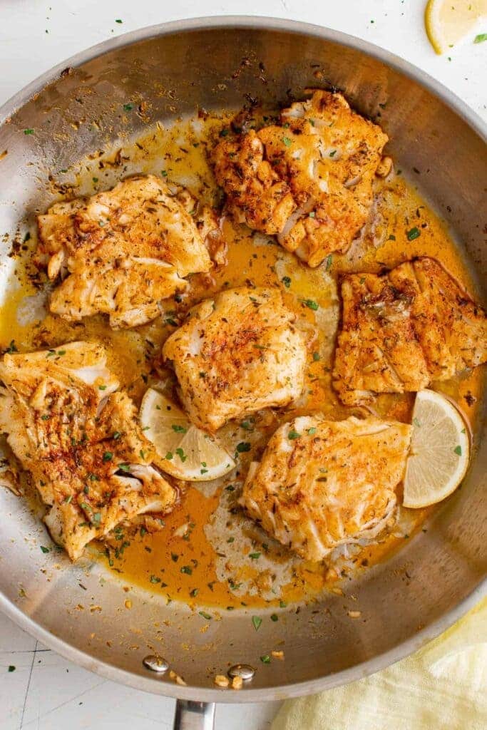 cod fish being fried in a pan with lemon wegdes