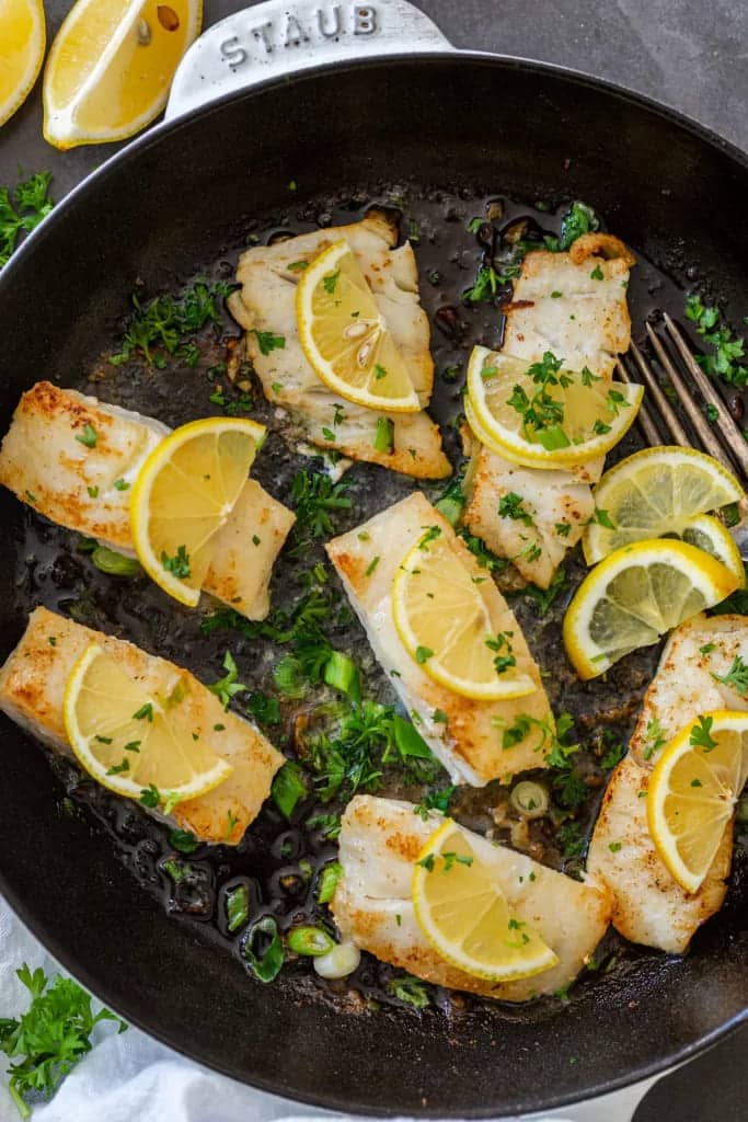 cod fish in a pan with lemon wedges and cilantro