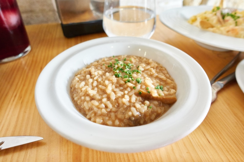 Tapa with boletus risotto and chopped chives in a white plate on a wooden table in a restaurant