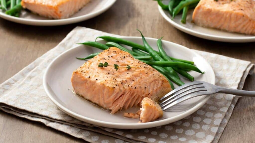 a small chunk of salmon placed in a white plate with green chillies