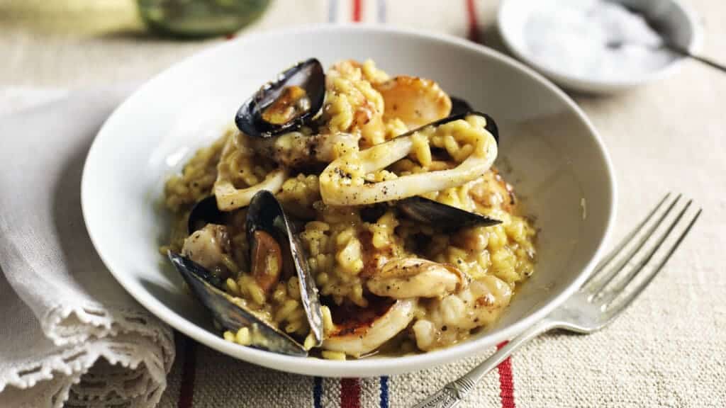 bowl of seafood risotto with a fork and napkin on both sides