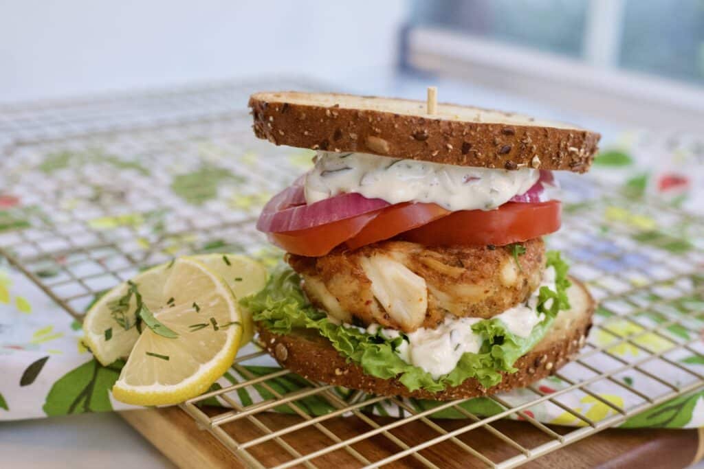 crab cake sandwich on a grill along with lemon slices and herbs