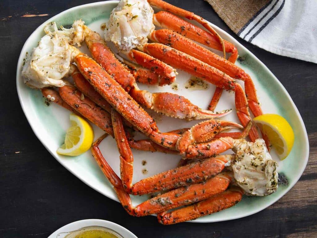 crab legs in a tray garnished with parsley lemon wedges on side