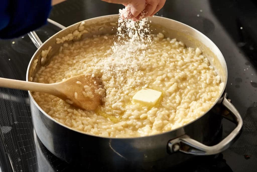 risotto in process zoomed in view of hand sprinkling cheese on the creamy rice in a pot