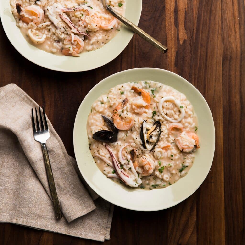 seafood risotto in white placed fork and napkin placed on the table