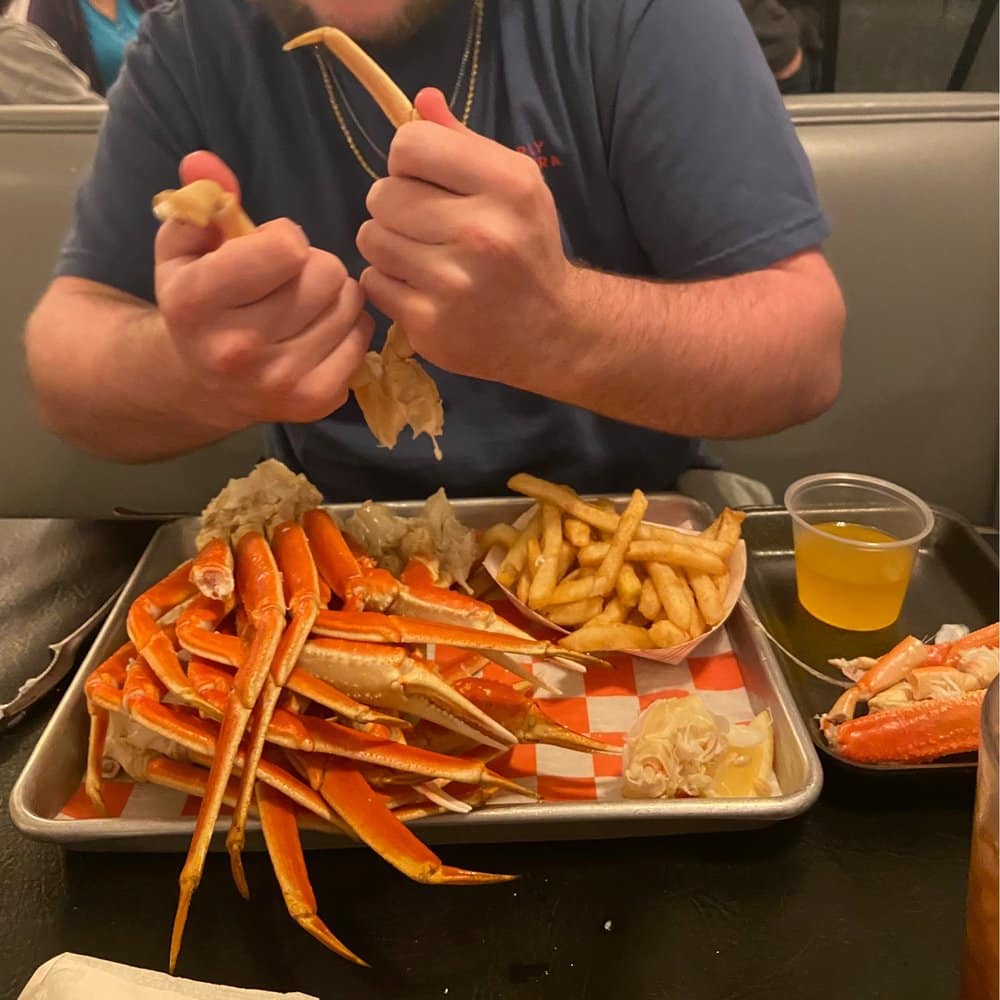 zoomed in view of hands holding crab legs with fries