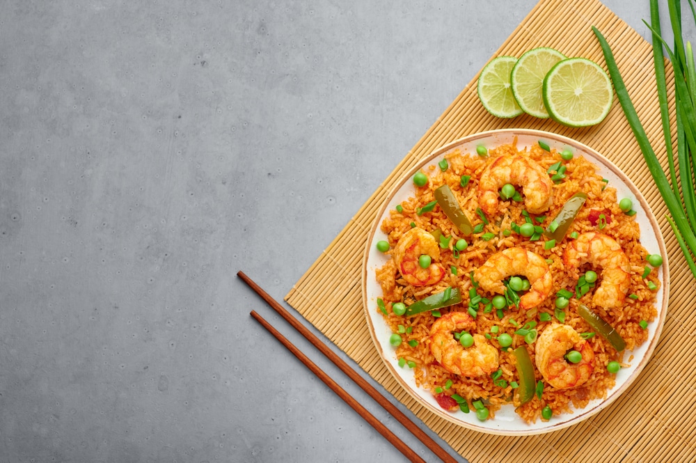 rice with shrimps and peas served in a dish along with green onion and lemon wedges