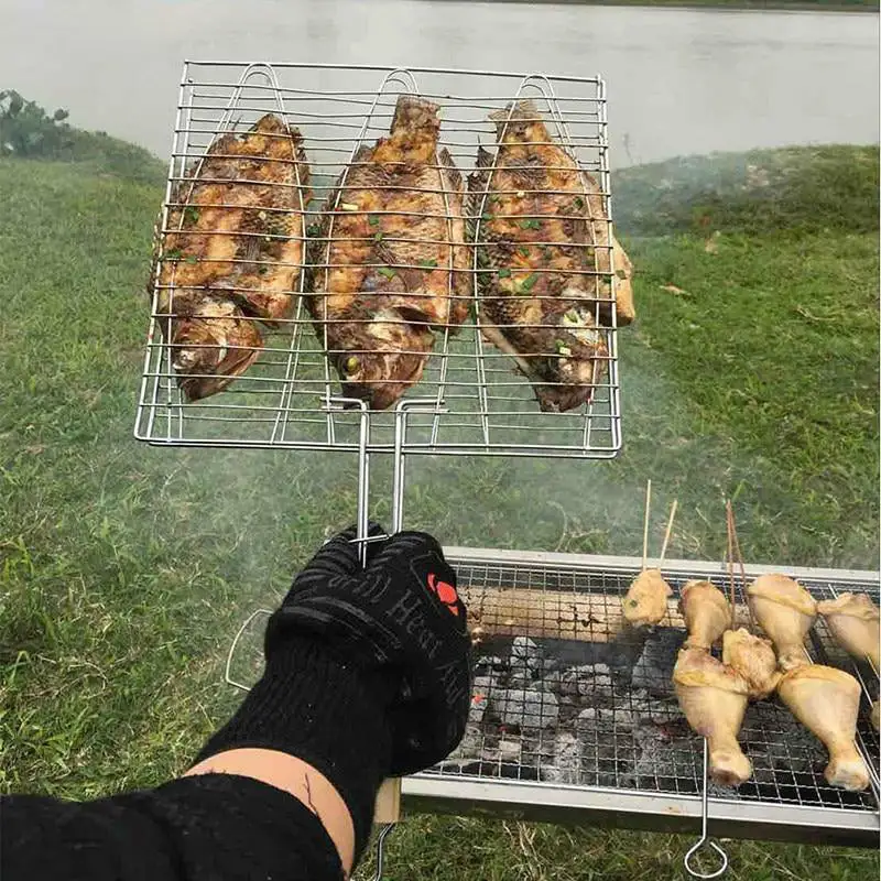 zoomed view of a hand with cooking mits on holding a grilling rack with - fish