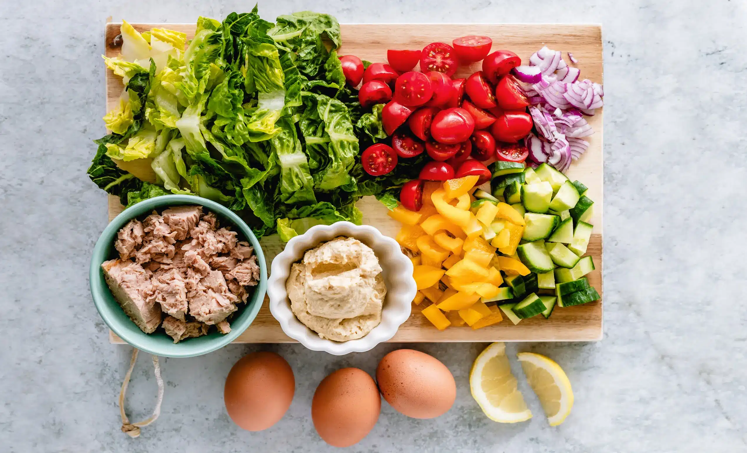 Fresh tuna salad ingredients with lettuce tomatoes cucumbers peppers red onions eggs and hummus