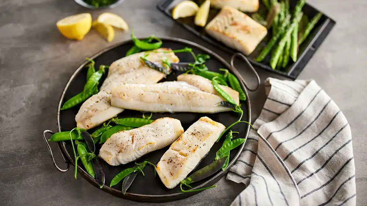 white fish fillets in a pan with pea garnishing